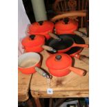 Seven orange Le Creuset pans.