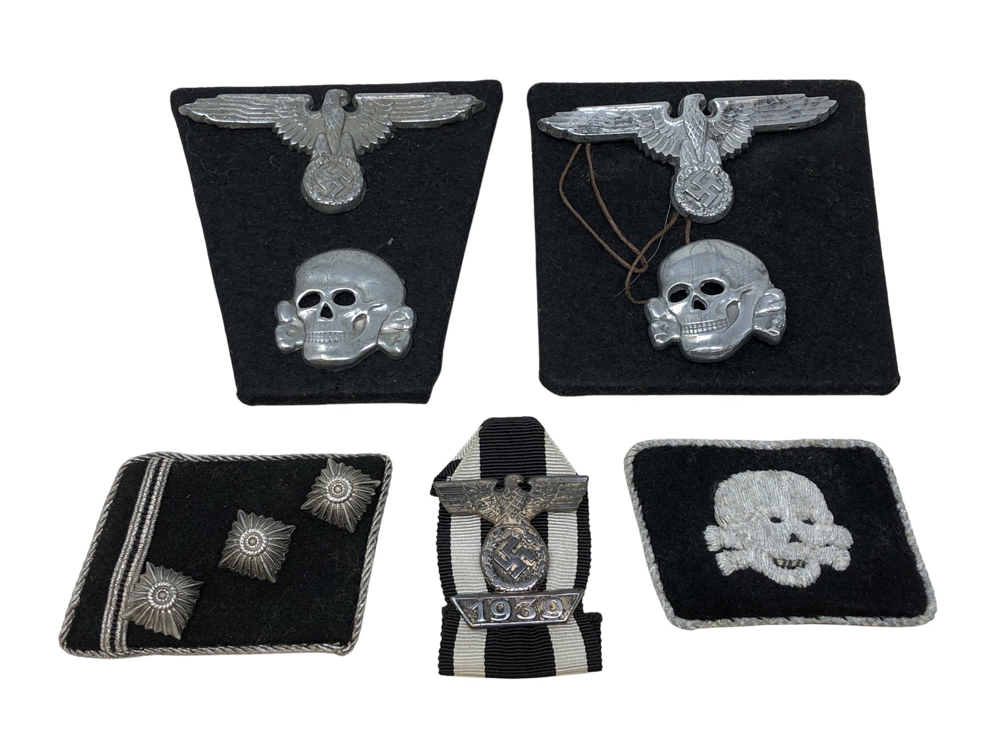 A group of German insignia including two Totenkopf skull cap badges, two eagle cap badges,
