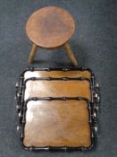 A graduated set of three ebonised twin handled serving trays together with a wooden tripod stool