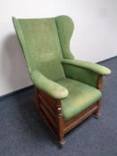 An Edwardian oak framed wingback rocking chair upholstered in a green fabric
