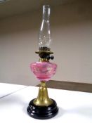 A 19th century brass oil lamp with hand painted pink glass reservoir chimney