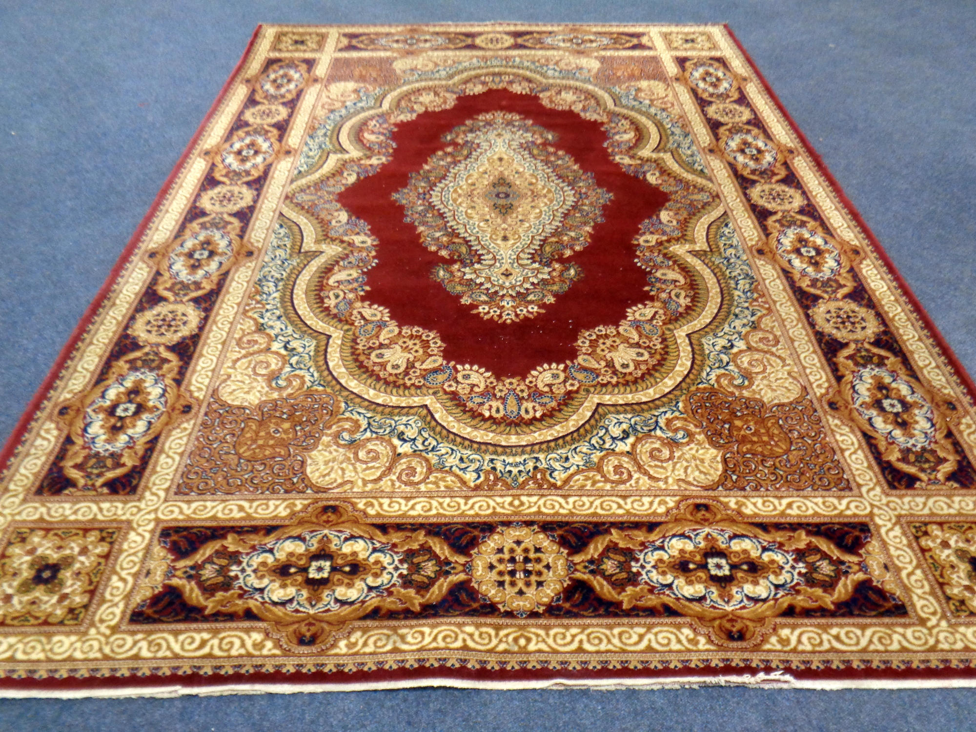 A machine made woolen rug with central medallion on red ground,