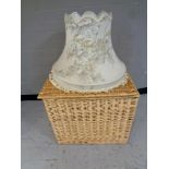 A large wicker hamper together with a standard lamp shade