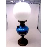 An antique brass oil lamp with blue glass reservoir, chimney and opaque glass shade,