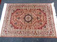 A fringed woolen rug of floral geometric design on pink ground,