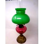 An antique brass duplex oil lamp with cranberry glass reservoir, chimney and green glass shade,