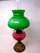 An antique brass duplex oil lamp with cranberry glass reservoir, chimney and green glass shade,