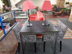 A black ash topped dining table on chrome legs together with a pair of contemporary armchairs and a