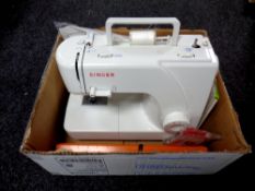 A box containing a Singer electric sewing machine with foot pedal and instruction manual together