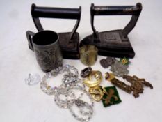 A box of two antique irons, plated napkin ring, pewter tankard, costume jewellery, military badges,