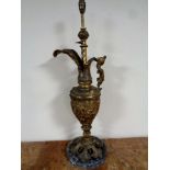 A gilded antique metal ewer with embossed decoration on marble plinth base, with cherub decoration,