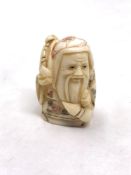 A Japanese craved bone netsuke : A village elder carrying wares on his shoulder.