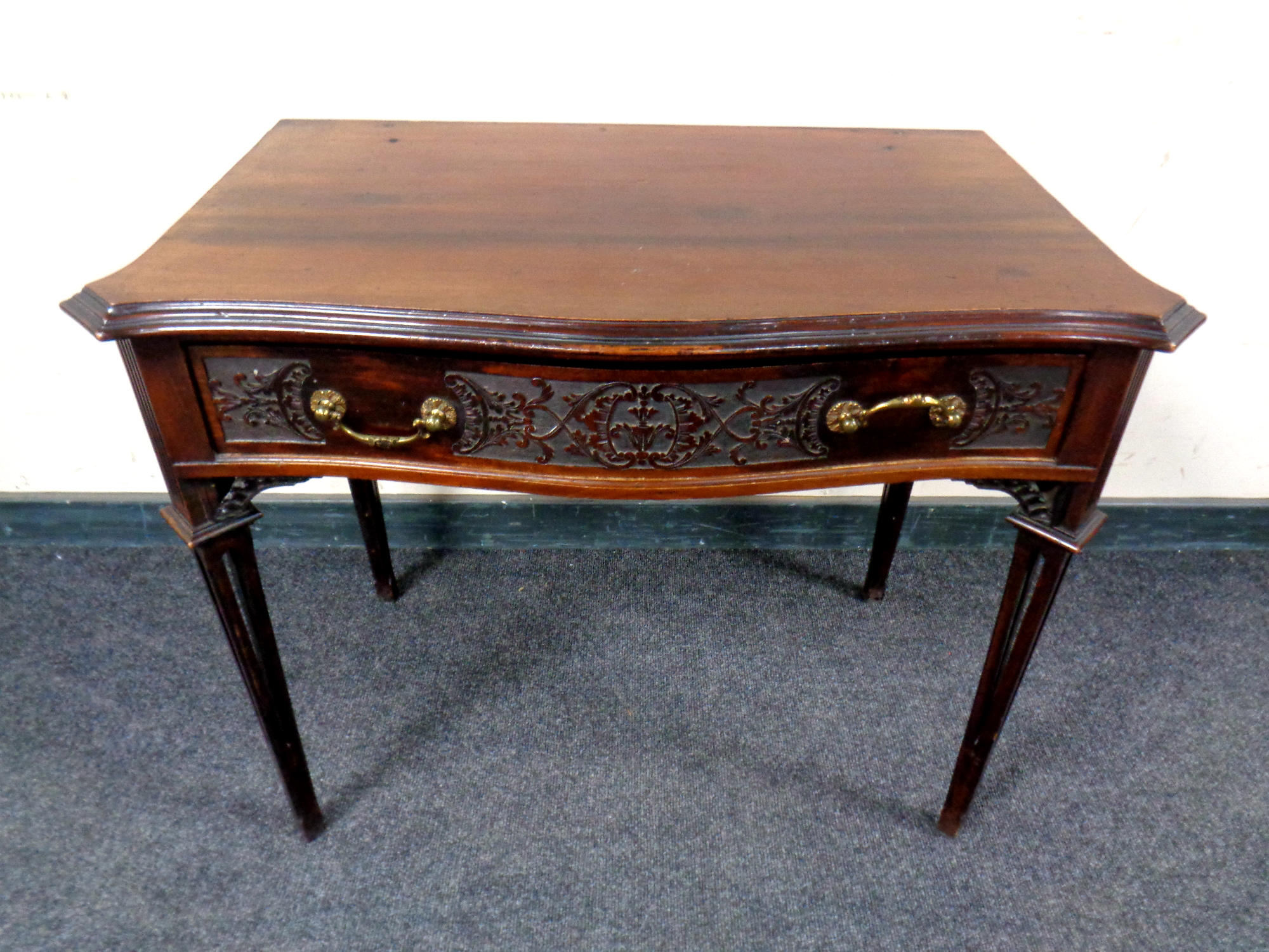 An Edwardian mahogany serpentine fronted side table fitted a drawer on reeded legs