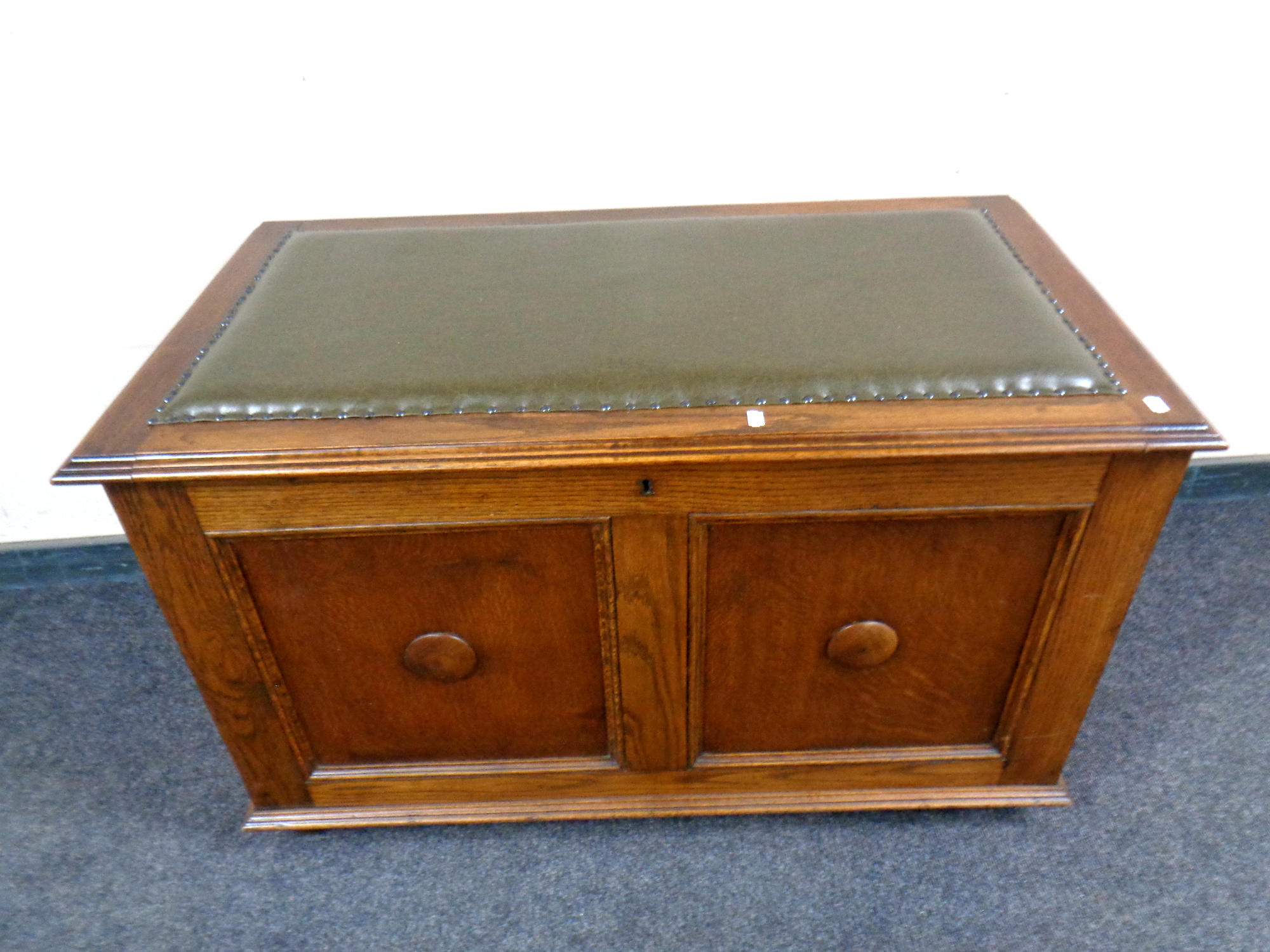 A twentieth century oak panelled blanket box with green buttoned cushion seat,