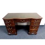 A mahogany serpentine fronted nine drawer desk with green tooled leather inset panel, width 115 cm.