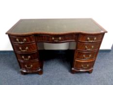 A mahogany serpentine fronted nine drawer desk with green tooled leather inset panel, width 115 cm.