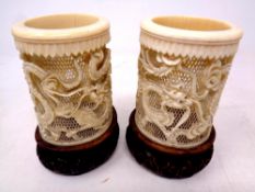 A pair of 19th century carved ivory brush pots depicting dragons on carved wooden bases,