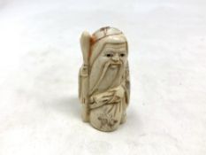 A Japanese carved bone netsuke - Village elder with a sack at his feet.