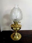 An antique brass oil lamp with glass chimney and frosted glass shade