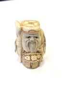 A Japanese carved bone netsuke - Village elder with a basket at his feet.