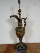 A gilded antique metal ewer with embossed decoration on marble plinth base, with cherub decoration,