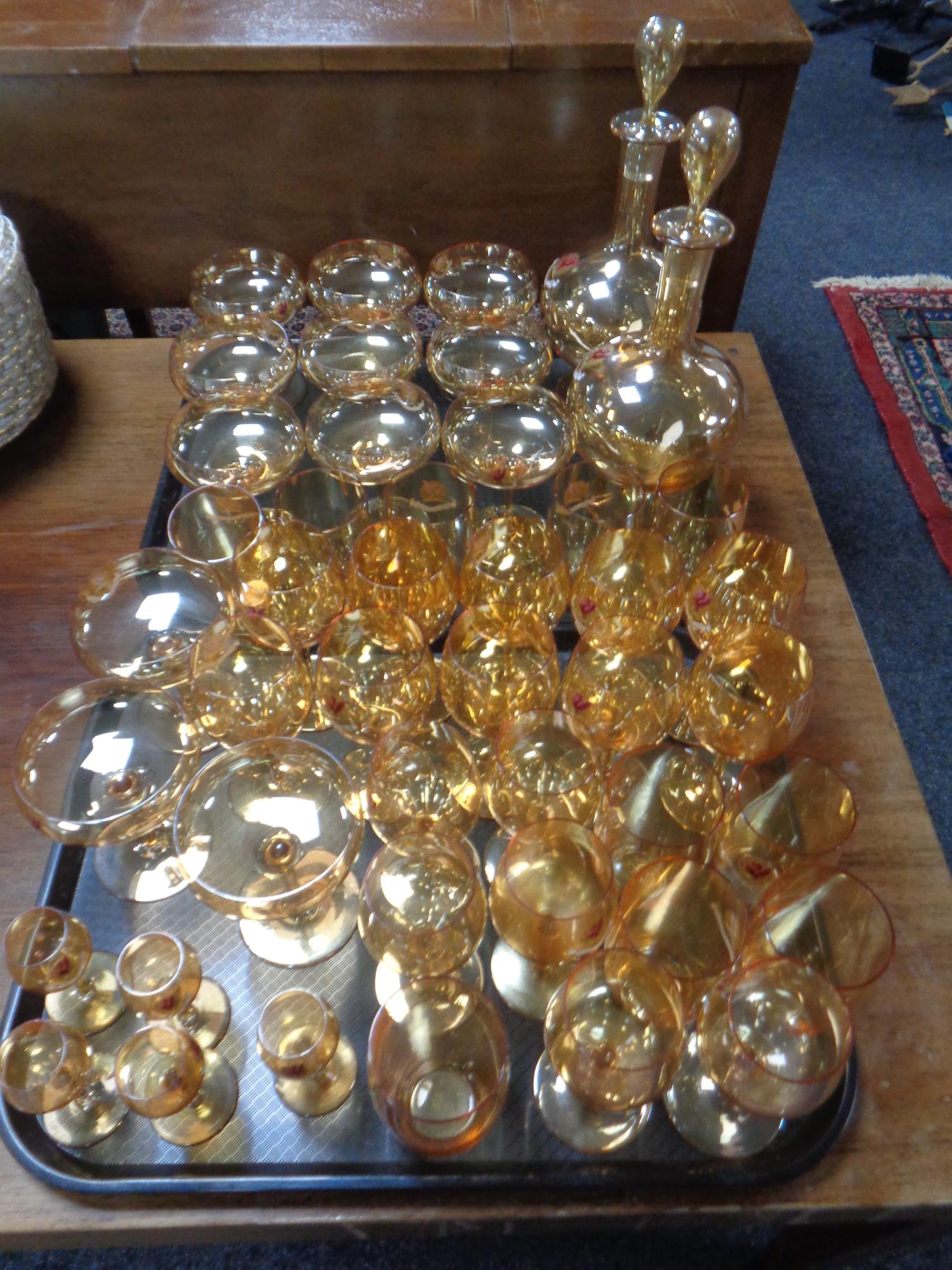 A pair of amber glass liqueur decanters together with a suite of glasses bearing dragon emblem,