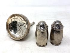 A pair of silver pepper pots, height 6 cm, together with a white metal wine strainer.