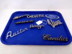 A tray containing eight car badges to include Ford Austin,