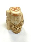 A Japanese carved bone netsuke - Village elder with a basket at his feet.