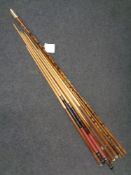 A vintage three piece bamboo fishing rod together with seven assorted snooker cues