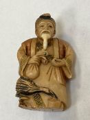 A carved Japanese netsuke depicting a man holding a money bag, height 65 mm.