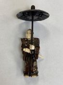 A carved Japanese netsuke modelled as a figure with parasol holding a sword, height 10 cm.