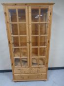 A pine double door glazed bookcase fitted three drawers beneath,