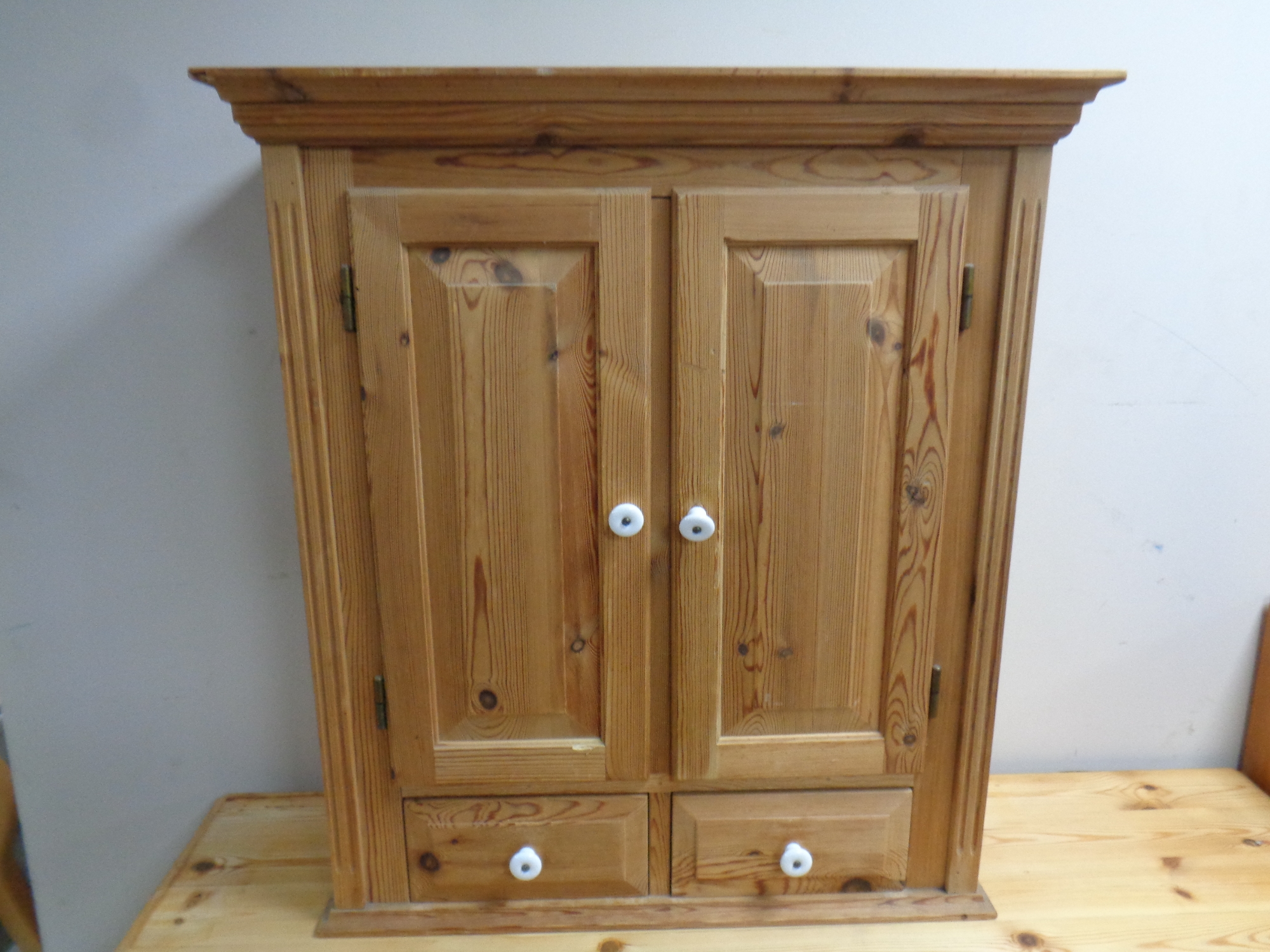 An antique pine double door hanging wall cabinet fitted two drawers beneath with porcelain handles