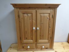 An antique pine double door hanging wall cabinet fitted two drawers beneath with porcelain handles