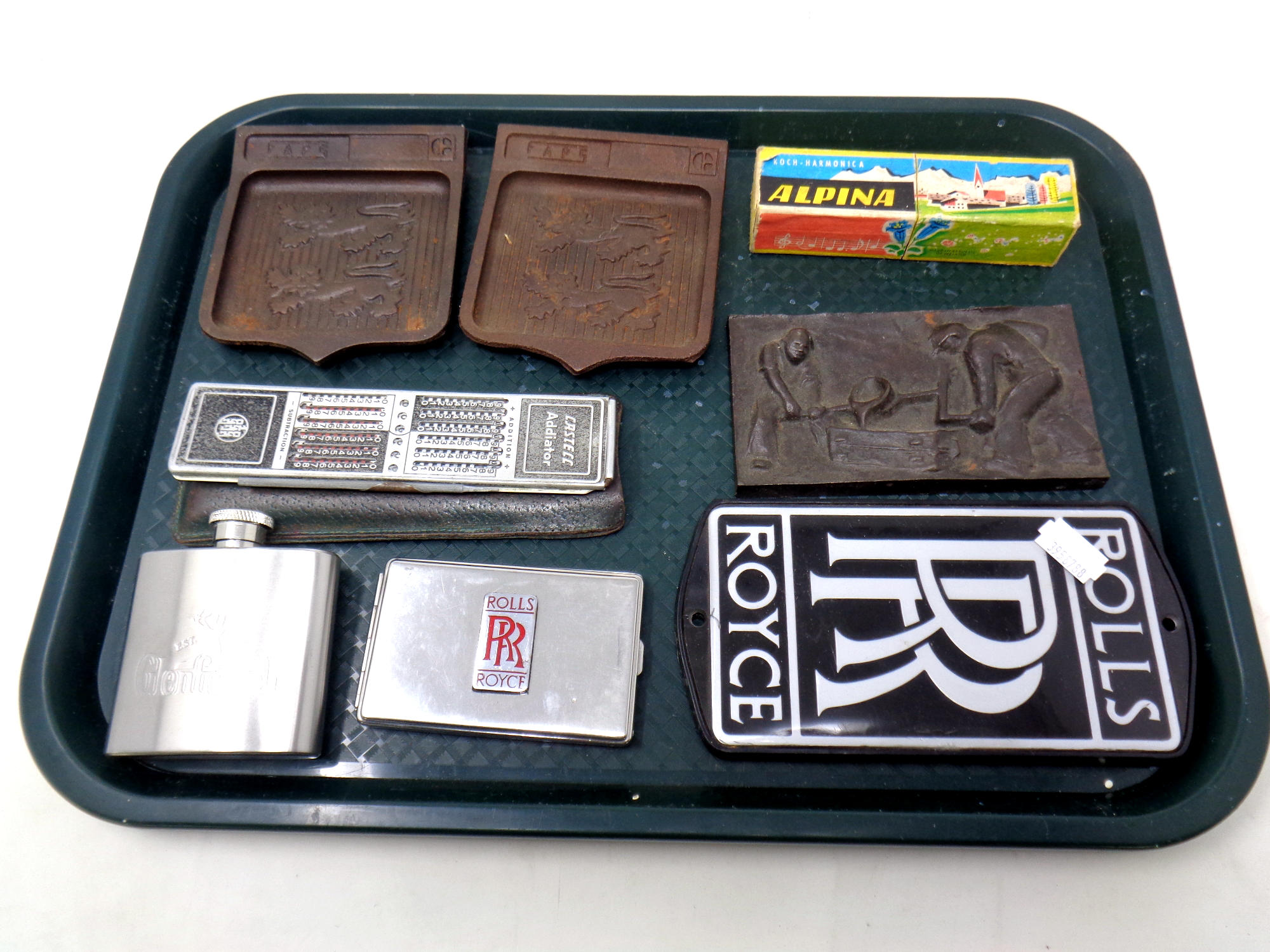 A tray of metal wares, Rolls Royce badges, Glenfiddich hip flask, embossed plaque, Castec Addiator,