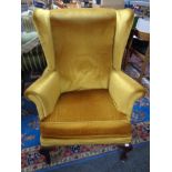 A 20th century wing backed armchair upholstered in gold dralon