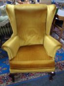 A 20th century wing backed armchair upholstered in gold dralon