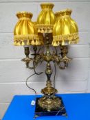 A decorative gilt metal five-way table lamp with gold tasseled shades on black marble base