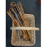 A large wicker log basket containing a quantity of assorted walking sticks and parasols including