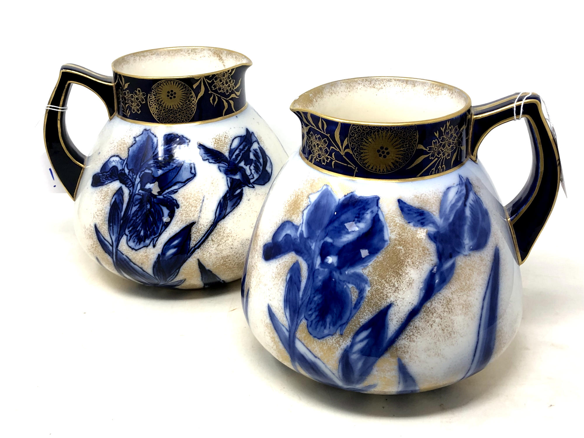 A pair of Art Nouveau Doulton Burslem blue and white iris pattern water jugs with gilt rims and
