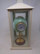 A hand painted ostrich egg clock with quartz movement on a figural base inside a hurricane lamp