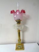 A brass Corinthian column oil lamp with etched cranberry glass shade,