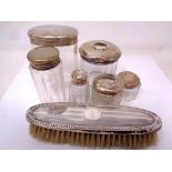 A small collection of silver topped dressing table jars and a silver backed dressing table brush.