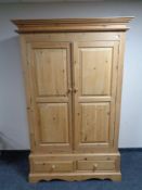 A stripped pine double door hanging wardrobe fitted two drawers beneath