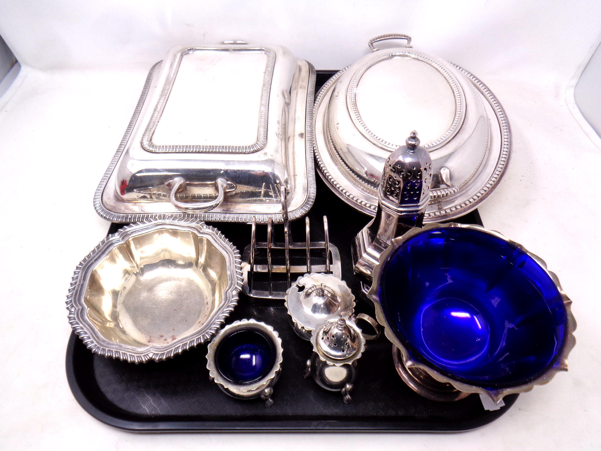 A tray containing silver plated items to include lidded entree dishes, cruet set, toast rack,