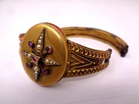 A Victorian pinchbeck bangle with central locket set with seed pearls and ruby-coloured stones (for