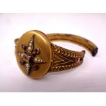 A Victorian pinchbeck bangle with central locket set with seed pearls and ruby-coloured stones (for