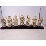 A set of seven Japanese carved bone figures on wooden stand