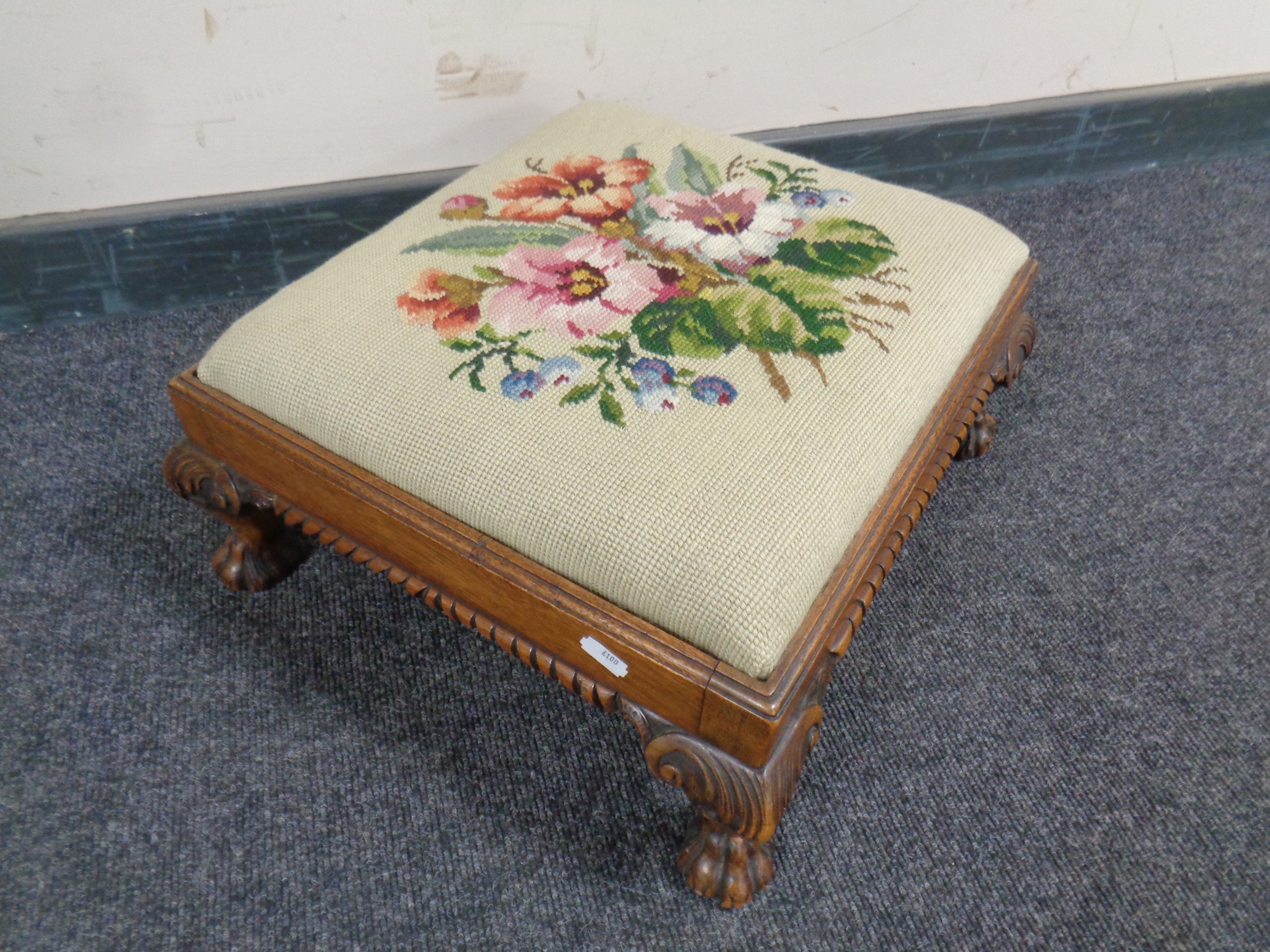 An embroidered footstool on carved lion paw feet